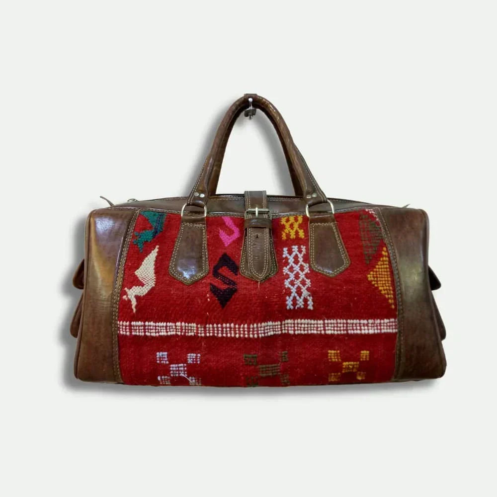 Travel bag with patterned red fabric and brown leather accents on a white background