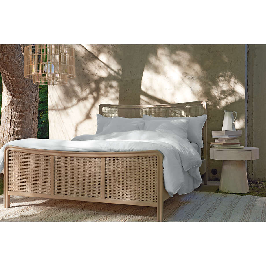 Bed with wicker frame in a natural setting with trees and a small table.