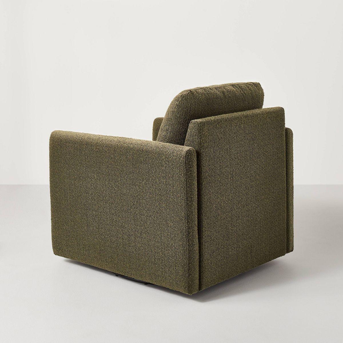 A greenish brown colored armchair with a textured fabric and square shape, placed on a light gray floor.
