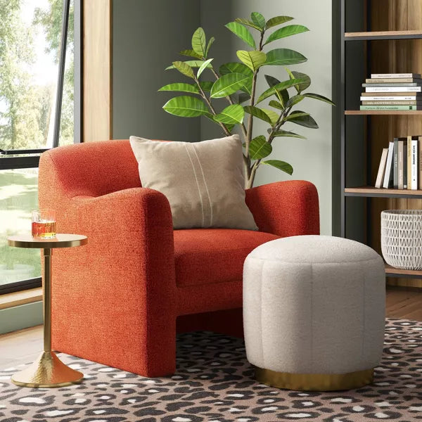 A round, cream colored ottoman with a textured surface and a gold colored base."