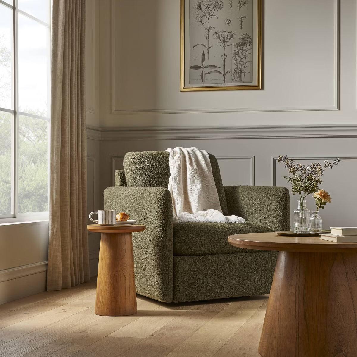 A greenish brown colored armchair with a textured fabric and square shape, placed on a light gray floor.