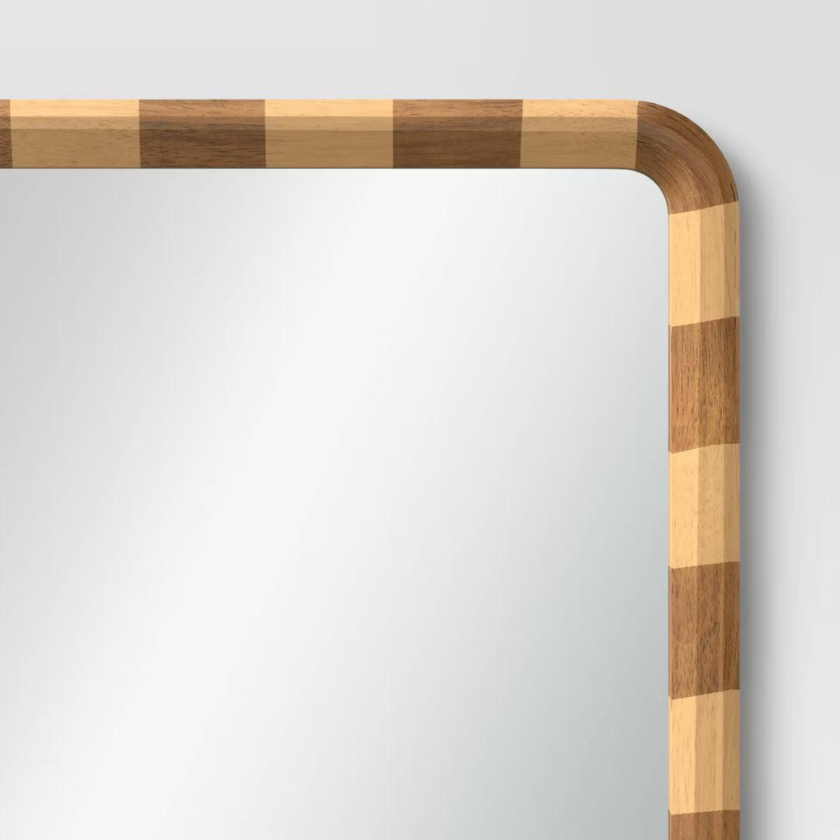 A mirror with a rounded corner and a checkered frame in alternating light and dark brown colored wood.