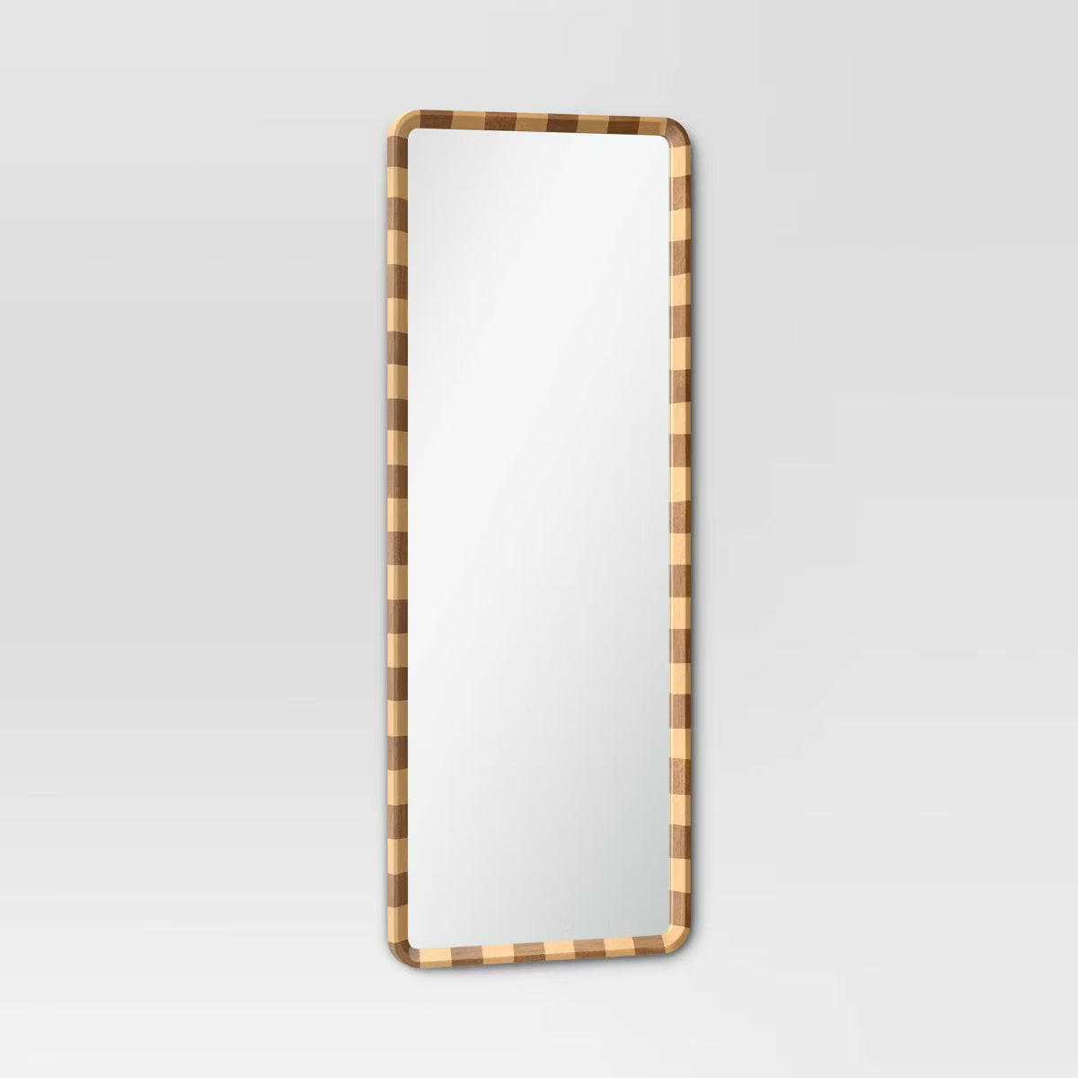 A mirror with a rounded corner and a checkered frame in alternating light and dark brown colored wood.