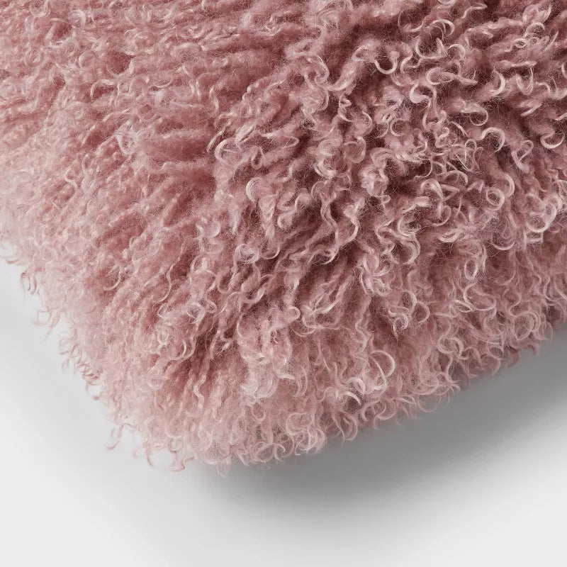 Close-up of a bed with burgundy quilt, pillows, and a fluffy pink pillow. Mauve