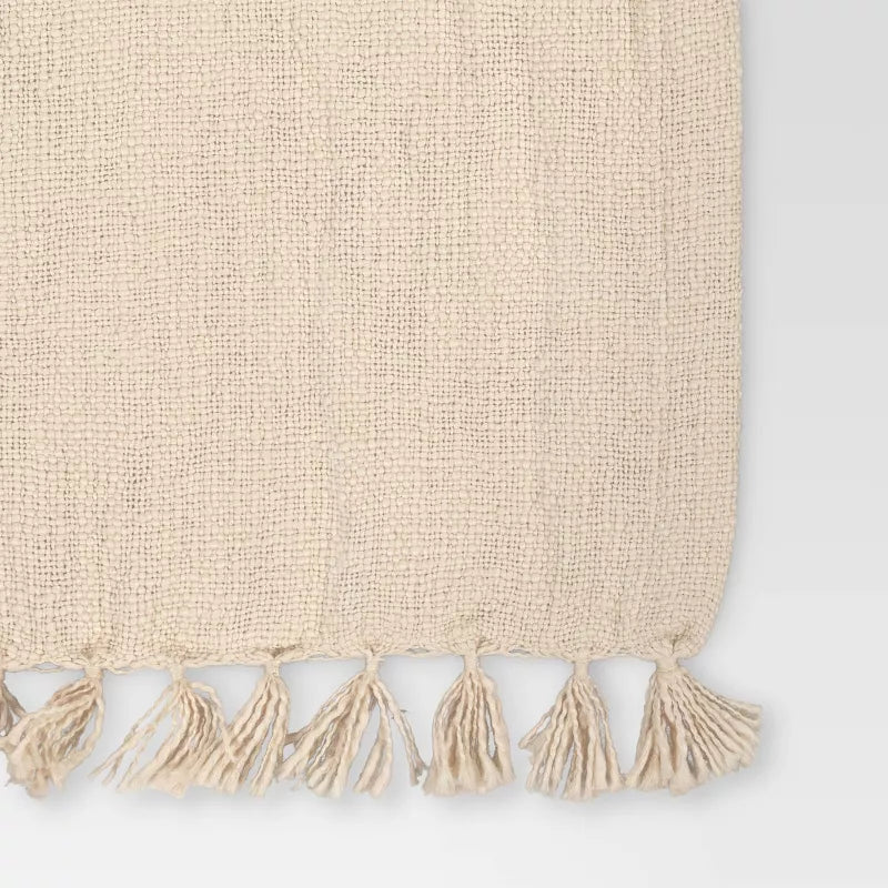 Beige woven blanket with tassels on a light gray background