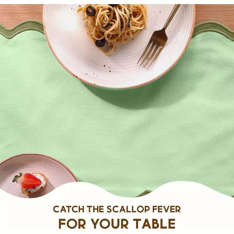 Green placemat with a plate of pasta and a fork on a wooden table.