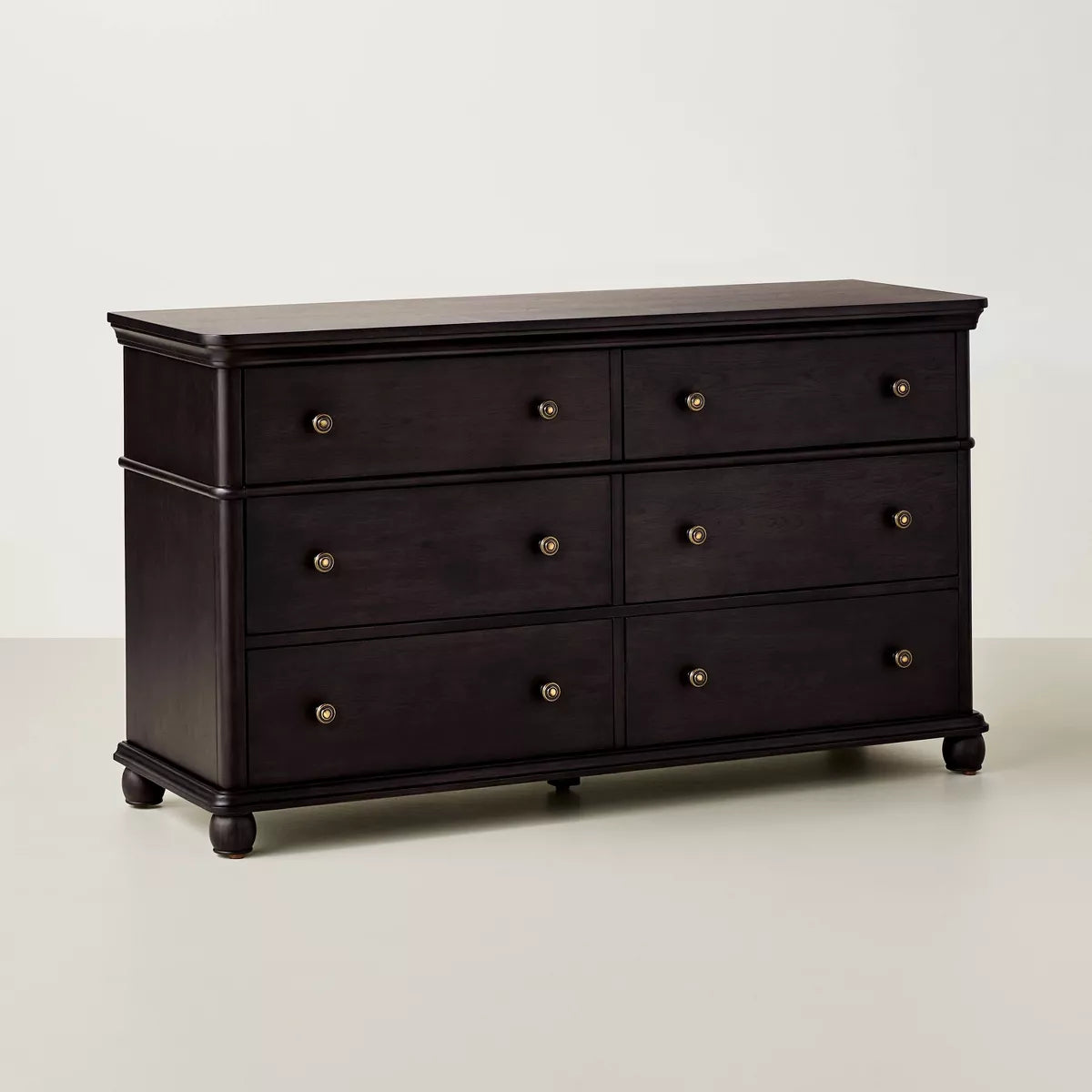A dark brown colored dresser with six drawers, featuring round knobs, is adorned with a white lamp, books, a bowl, and a candle holder on top Black.