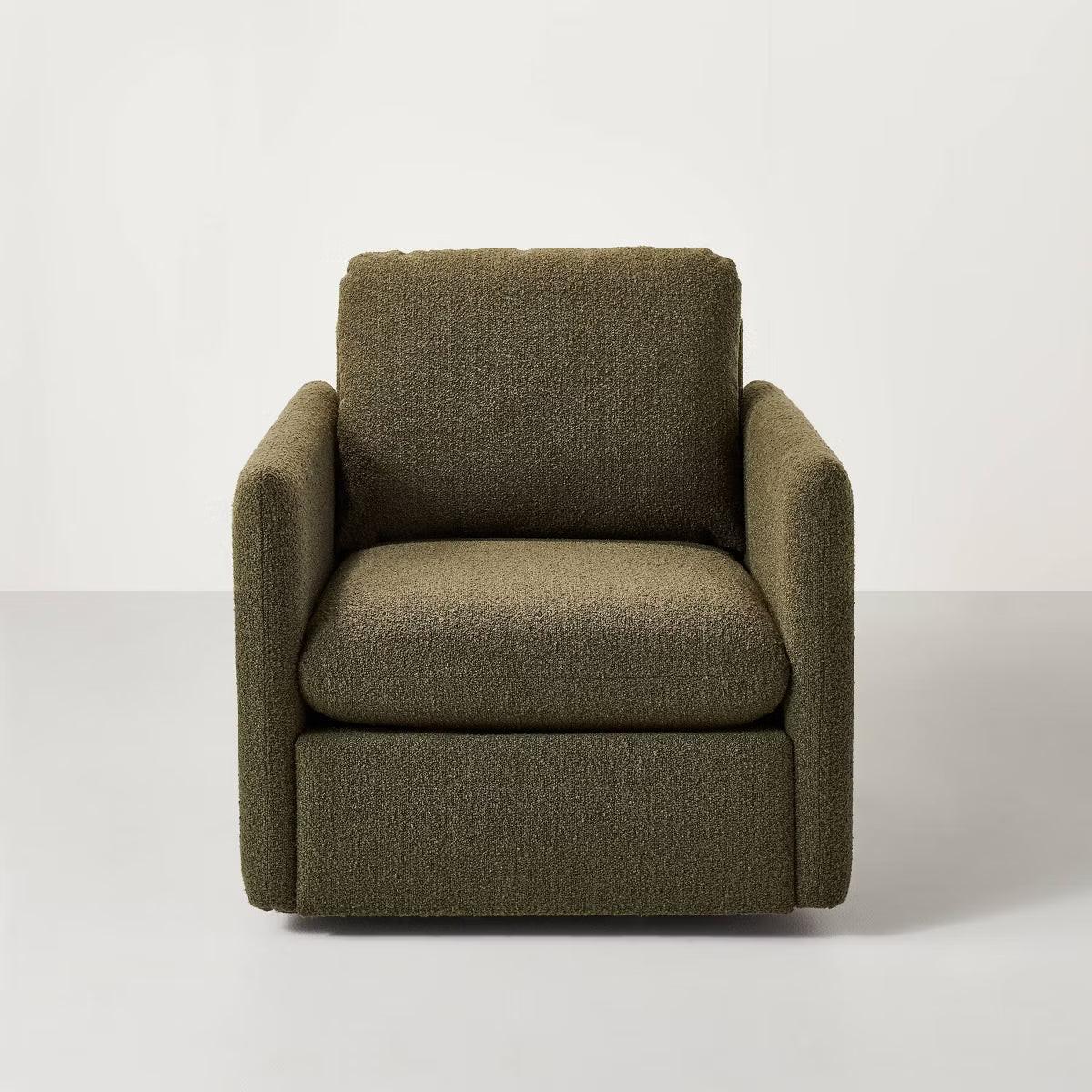 A greenish brown colored armchair with a textured fabric and square shape, placed on a light gray floor.