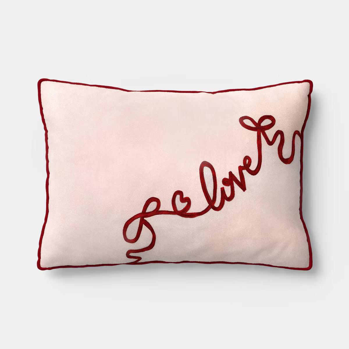 Rectangular light pink colored pillow with red colored piping and the word & quot love quot embroidered in red.