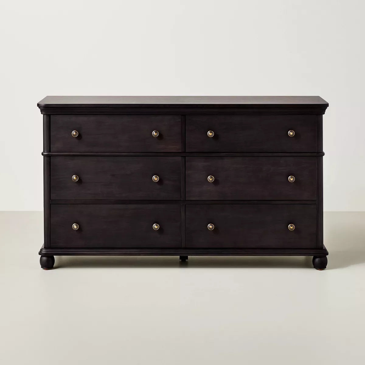A dark brown colored dresser with six drawers, featuring round knobs, is adorned with a white lamp, books, a bowl, and a candle holder on top Black.