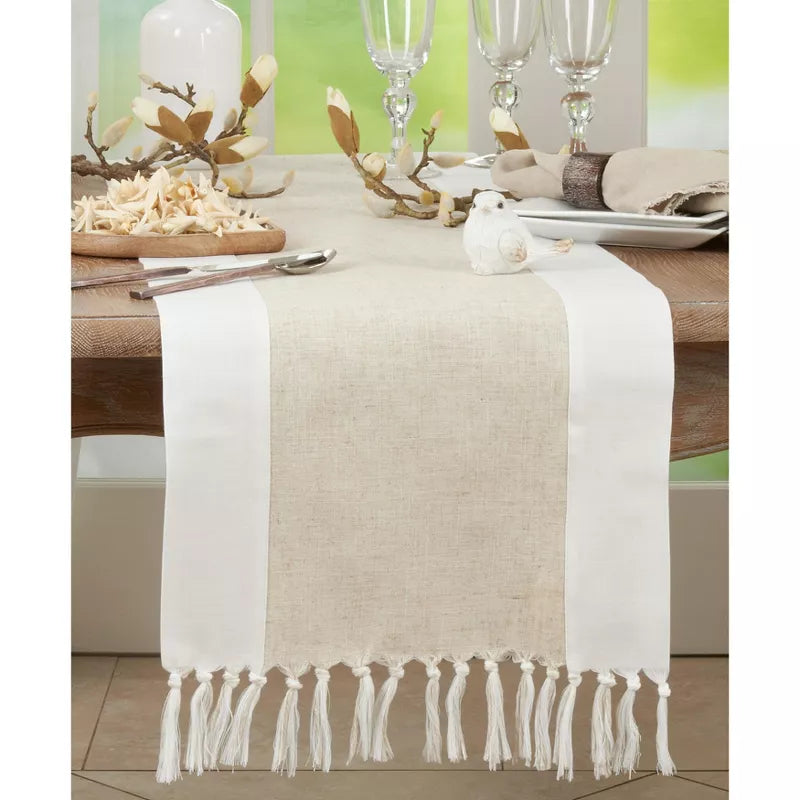 Beige and white table runner with fringe on a decorated table.
