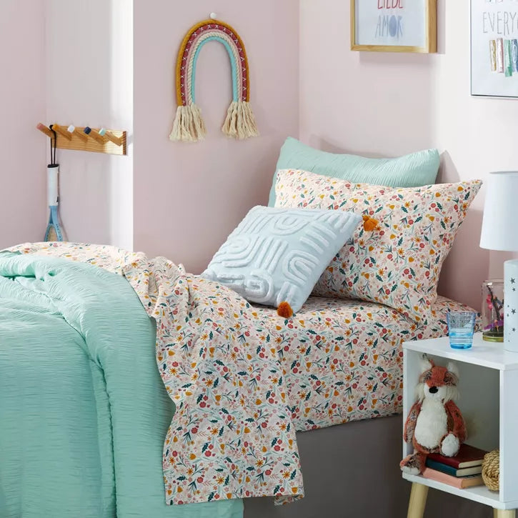 Bedroom with floral bedding and colorful pillows on a bed against a pink wall.