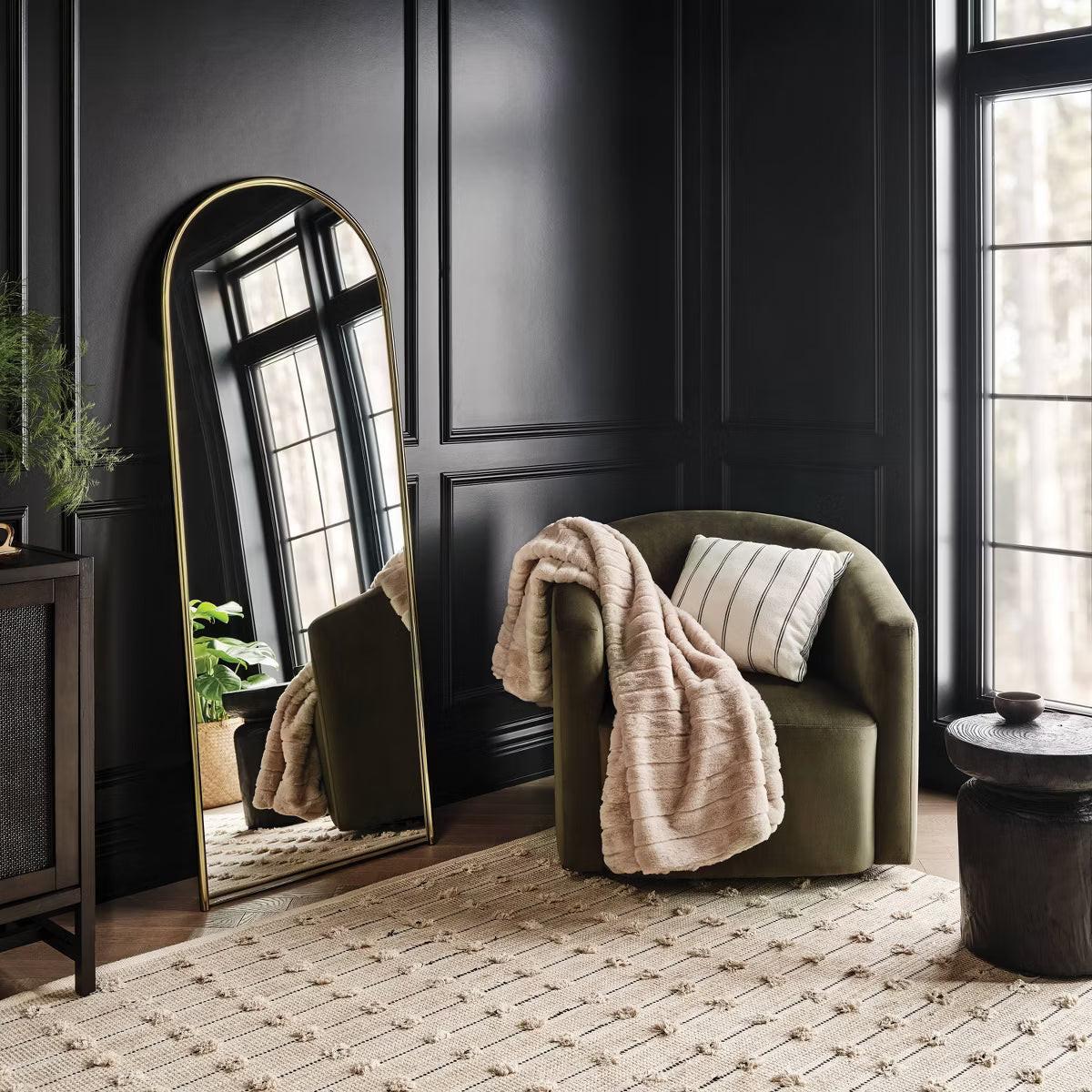 An arched mirror with a thin gold colored frame against a light gray background.