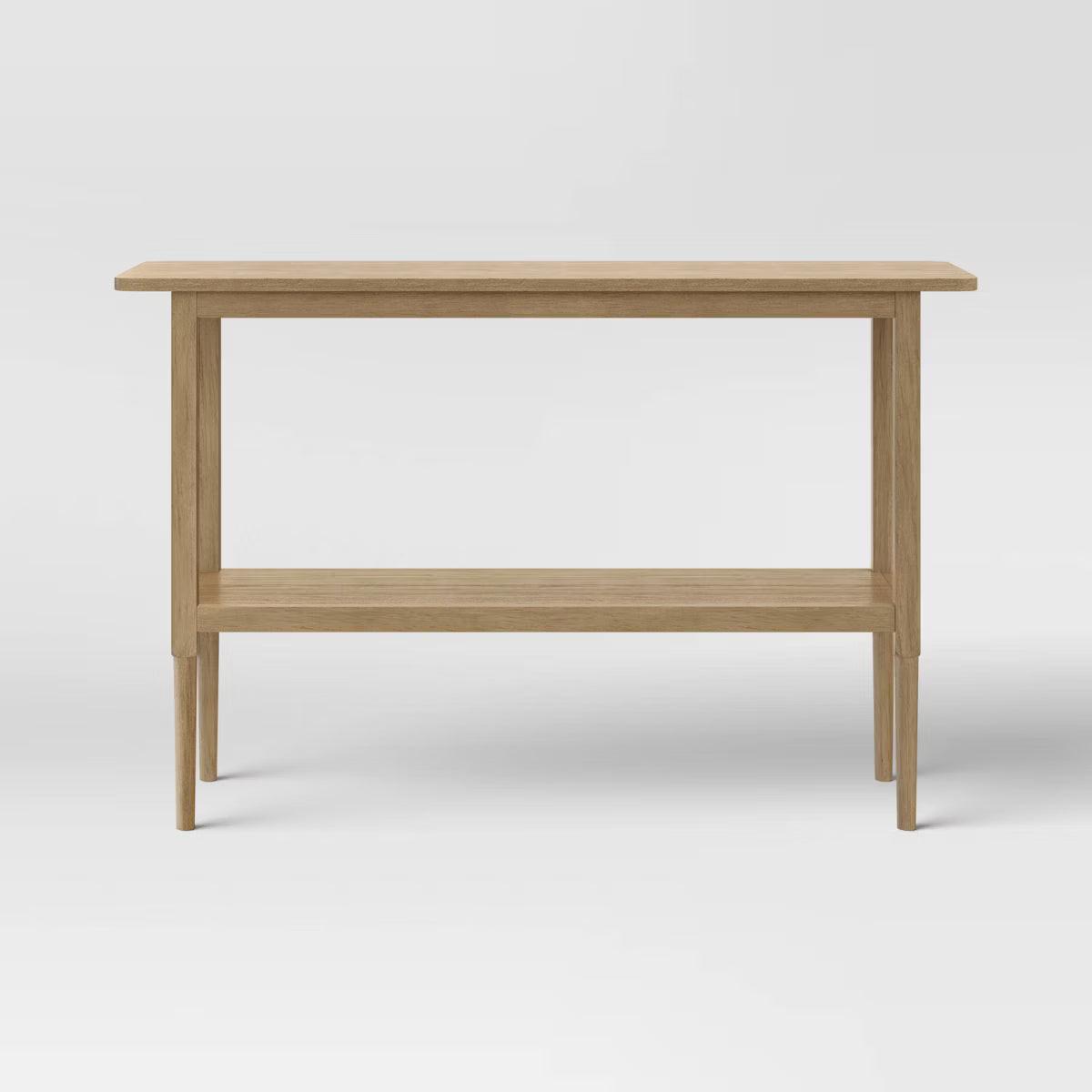 A light brown colored rectangular table with four slender legs and a lower shelf