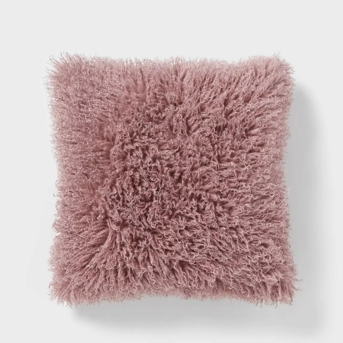 Close-up of a bed with burgundy quilt, pillows, and a fluffy pink pillow. Mauve