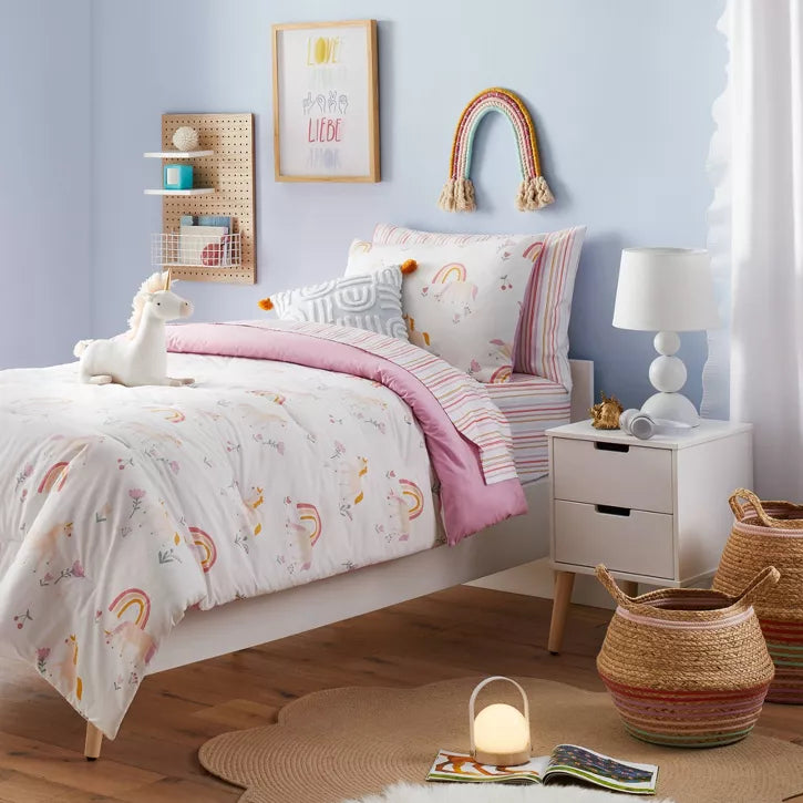 Bedroom with floral bedding and colorful pillows on a bed against a pink wall.