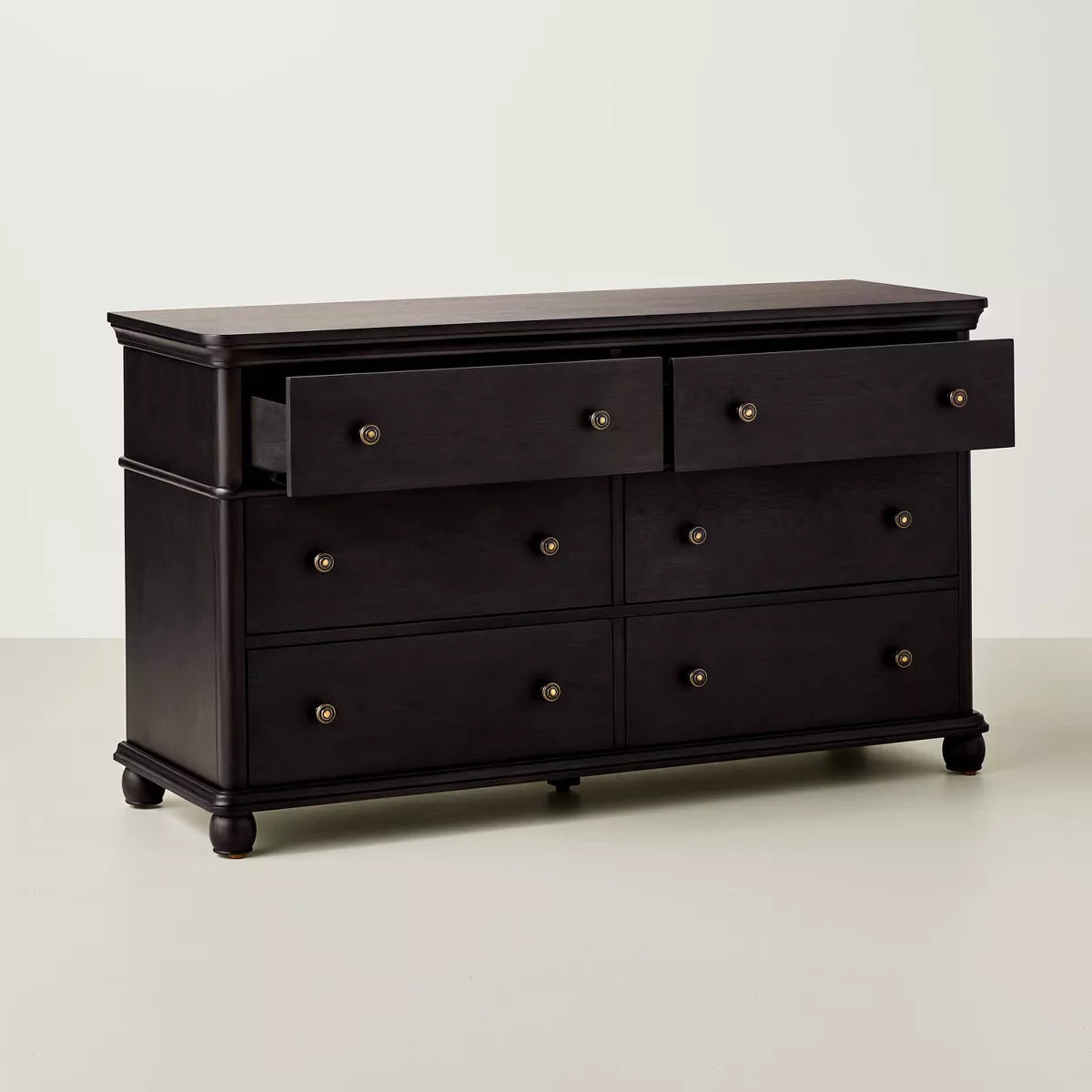 A dark brown colored dresser with six drawers, featuring round knobs, is adorned with a white lamp, books, a bowl, and a candle holder on top Black.