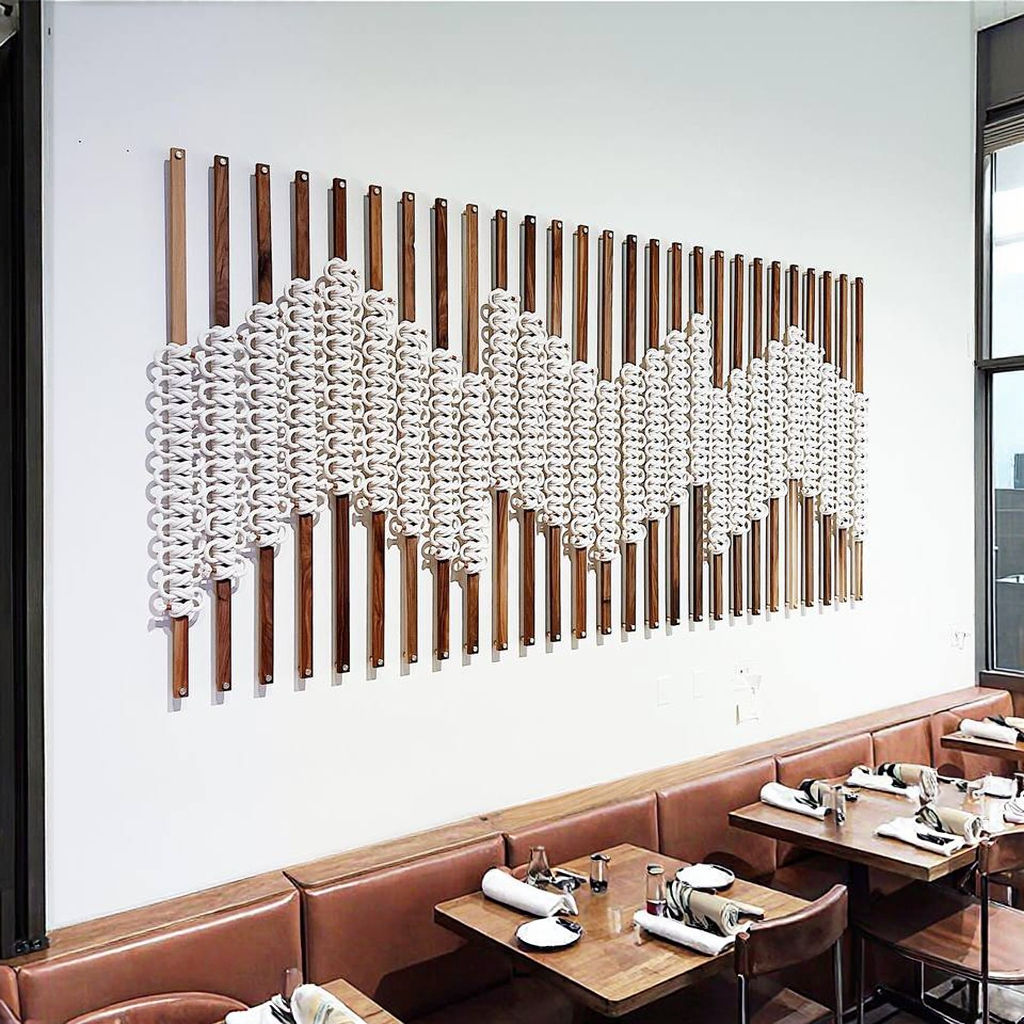 Modern interior design with a wall art piece featuring wooden slats and white spherical elements, adjacent to a dining area with brown leather booths.