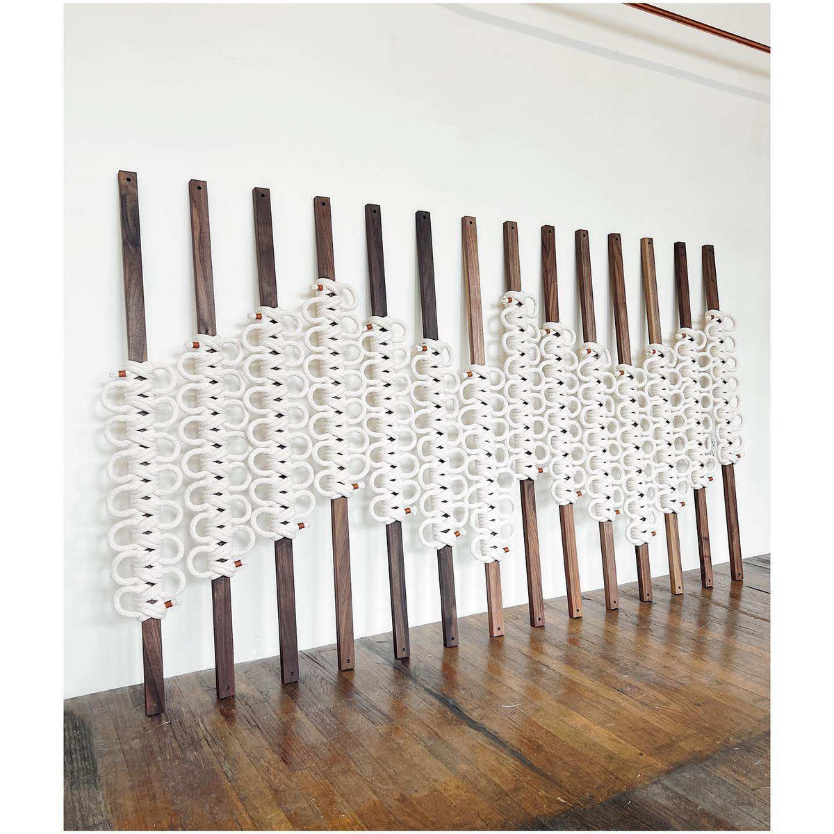 Decorative wall art with white geometric patterns on wooden sticks against a white wall.