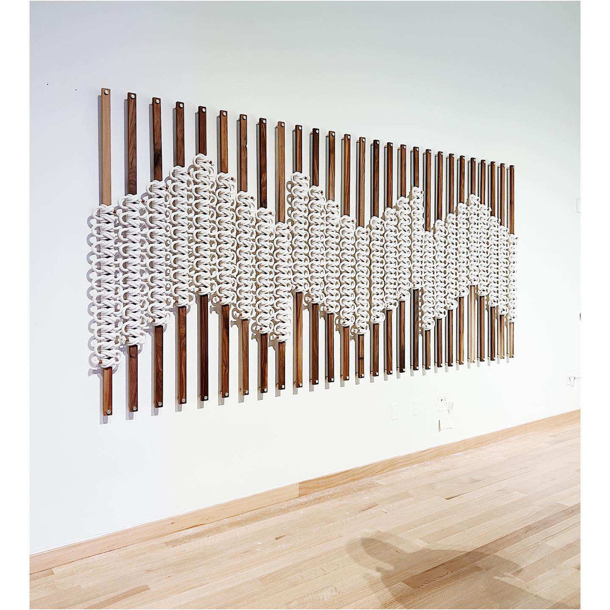 Wall-mounted art piece with wooden slats and white spherical elements on a light gray wall.
