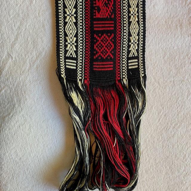Decorative belt with red, black, and beige patterns on a light background Authentic large woven faja from Cuanajo, Michoacán. Handwoven on a backstrap loom with traditional Purepecha designs. Cotton sash, 54" x 3.5" – wearable or decorative.