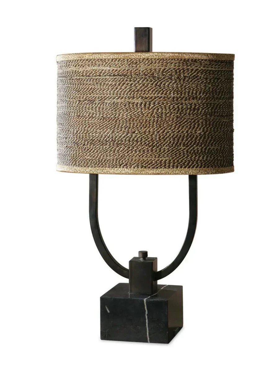 Rustic table lamp with burnished bronze body, black marble base, and a woven rattan oval drum shade with decorative trim.