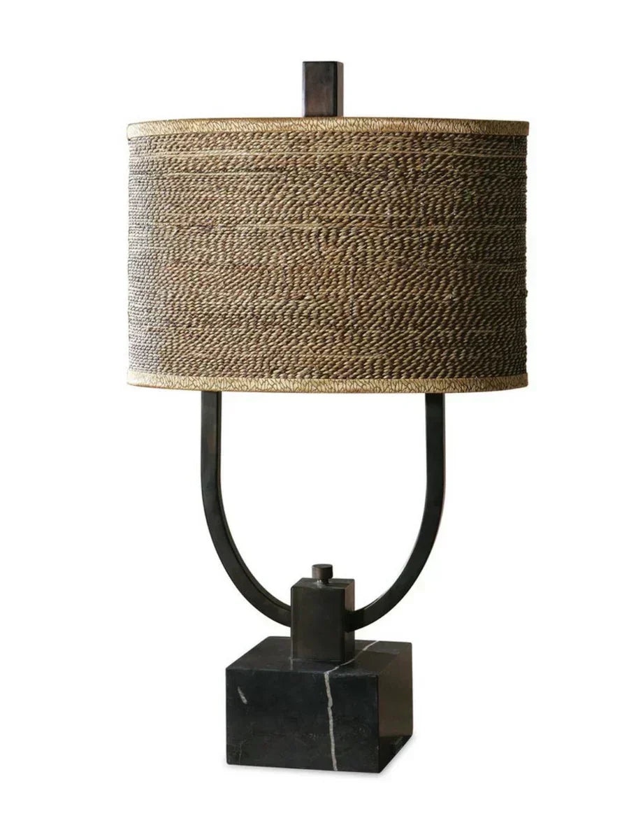 Rustic table lamp with burnished bronze body, black marble base, and a woven rattan oval drum shade with decorative trim.
