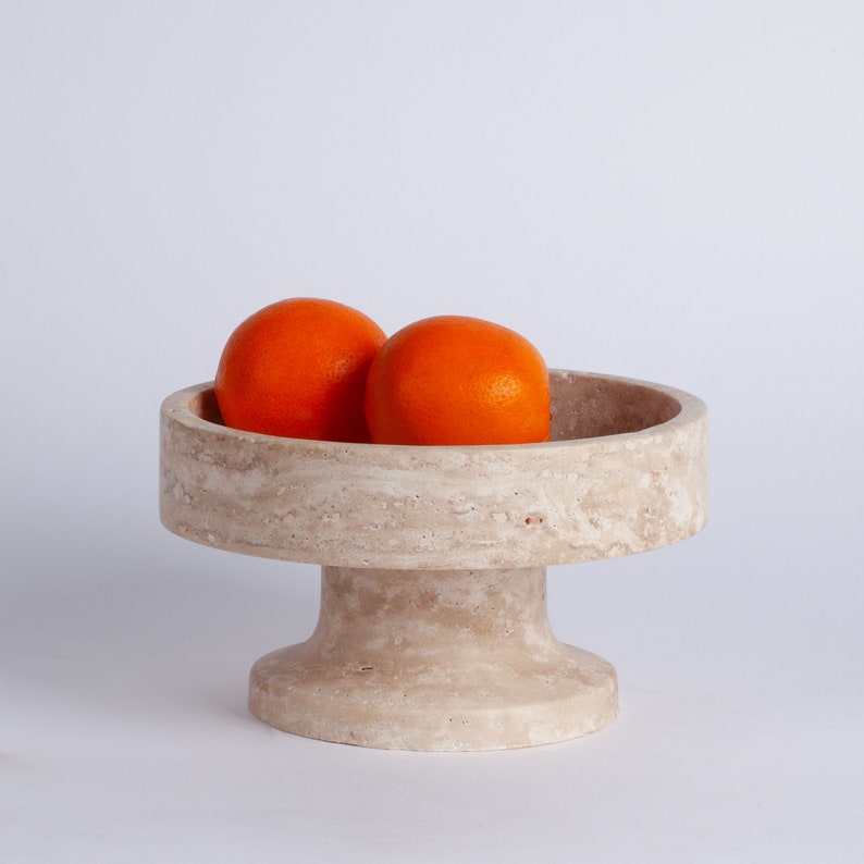 Marble pedestal bowl with two oranges on a light gray background