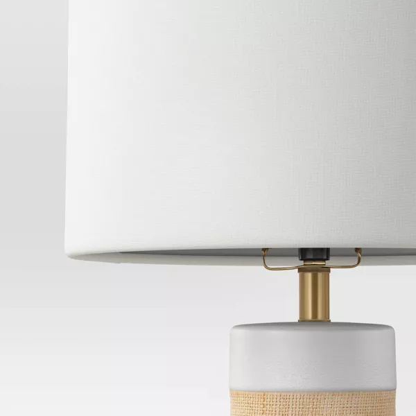 Table lamp with a white shade and woven design base on a light gray background