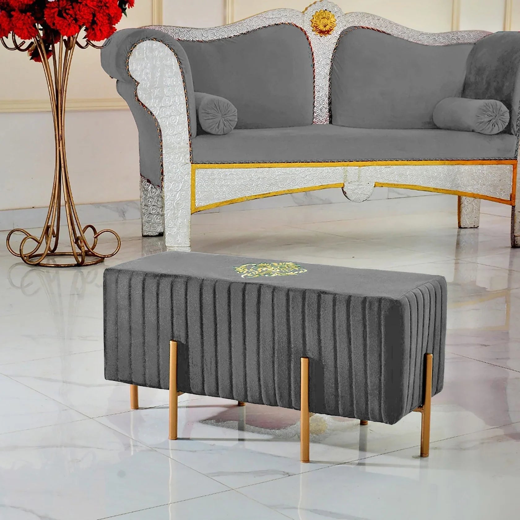 Gray upholstered bench with gold legs in front of a gray sofa with decorative armrests.