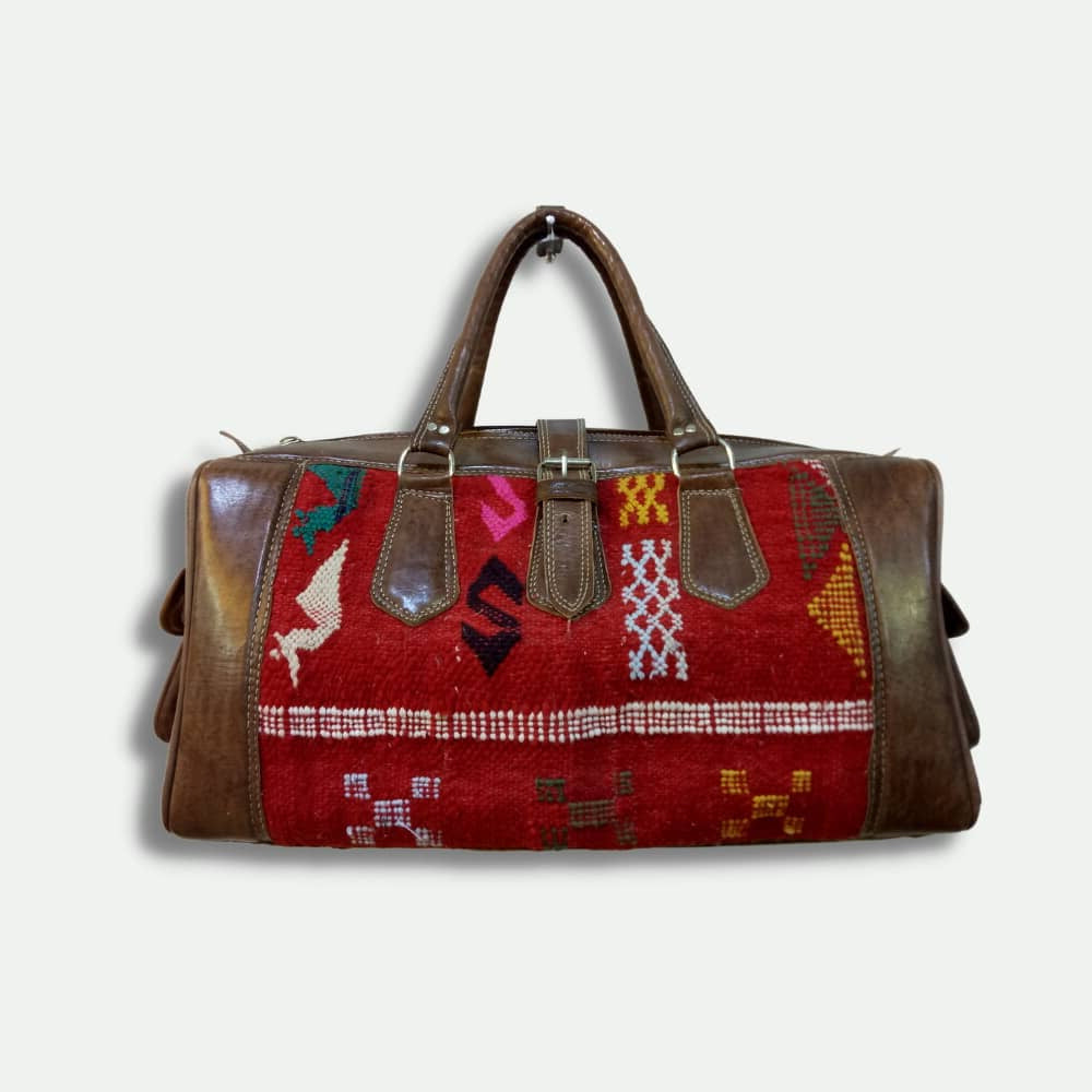 Travel bag with patterned red fabric and brown leather accents on a white background