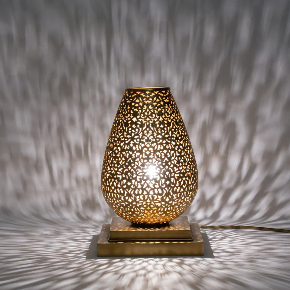 Decorative table lamp with intricate design casting shadows on a textured wall.
