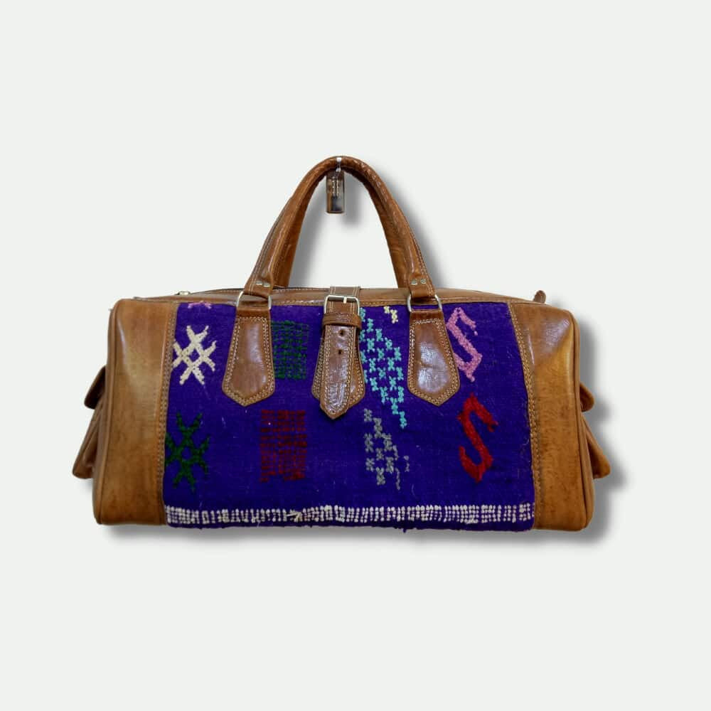 Brown leather duffel bag with a colorful patterned flap on a white background