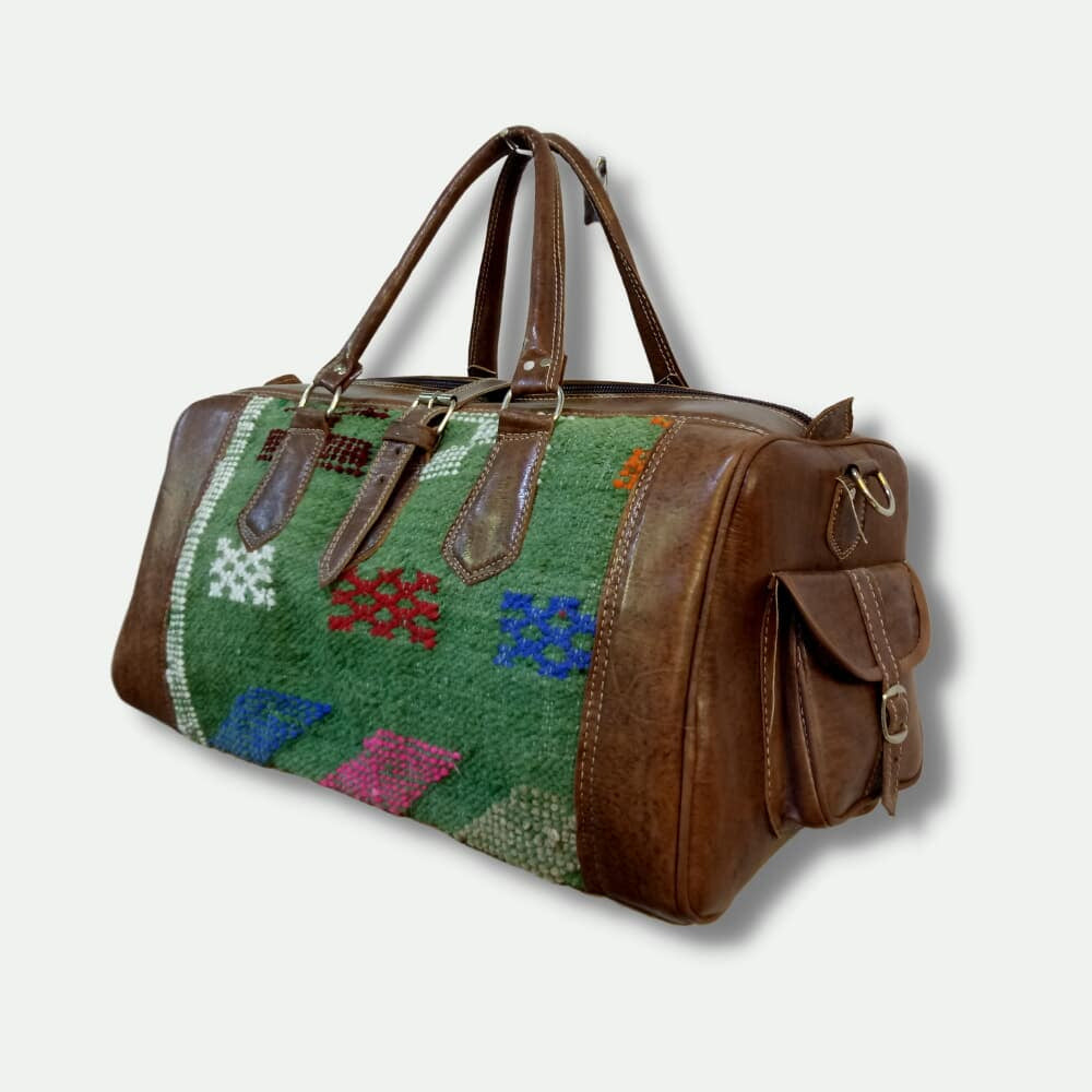 Multicolored patterned duffel bag with brown leather accents on a light gray background