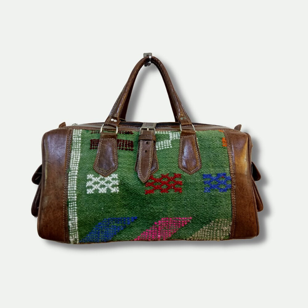 Travel bag with green patterned fabric and brown leather accents on a white background