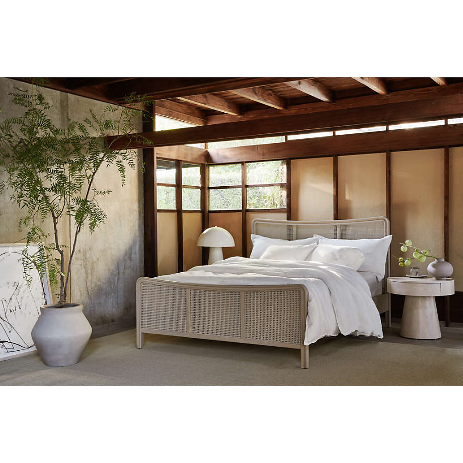 Beige rattan bed in a modern bedroom with wooden beams and large windows.