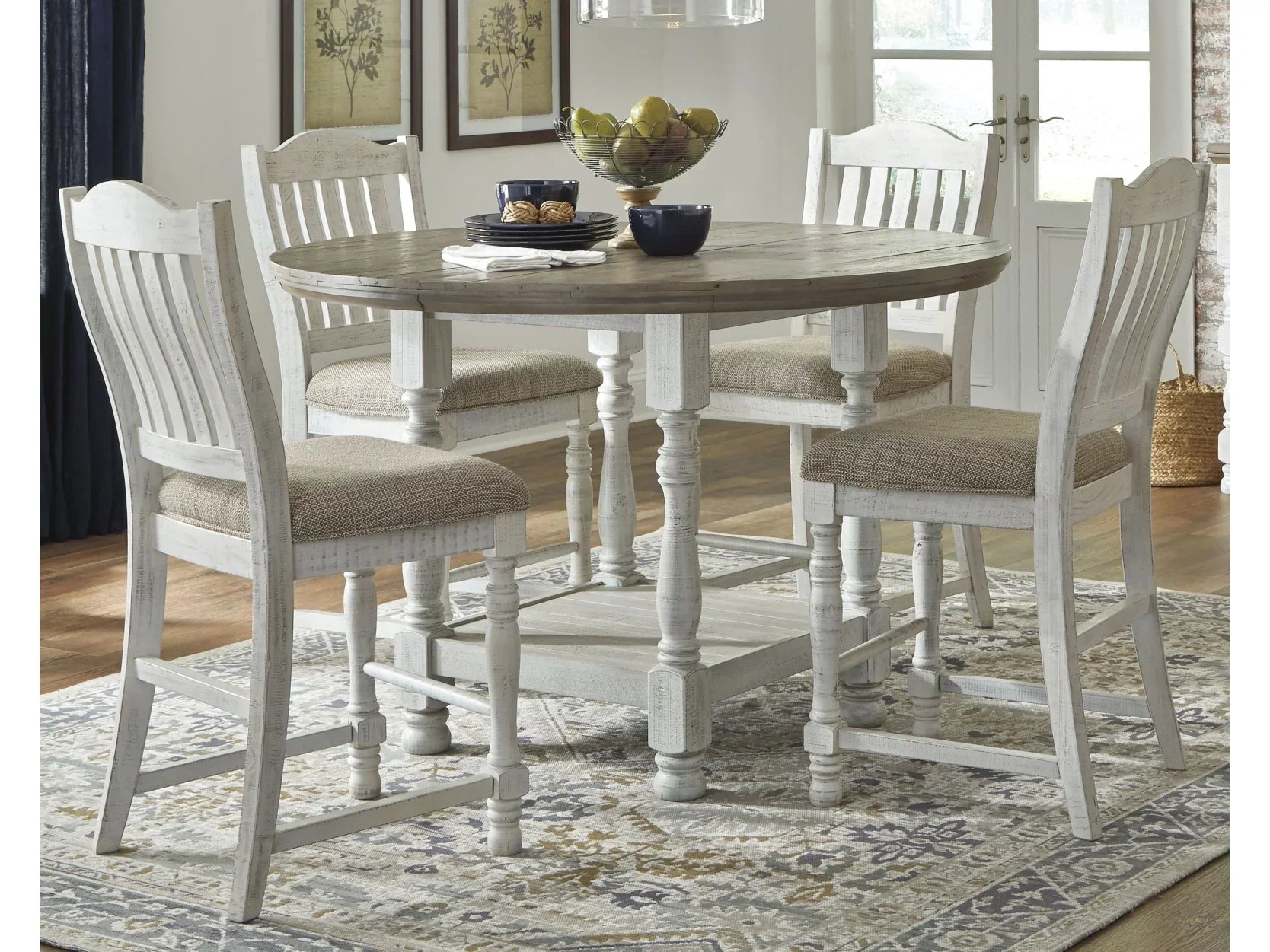 Dining room with a round wooden table and white chairs on a patterned rug.