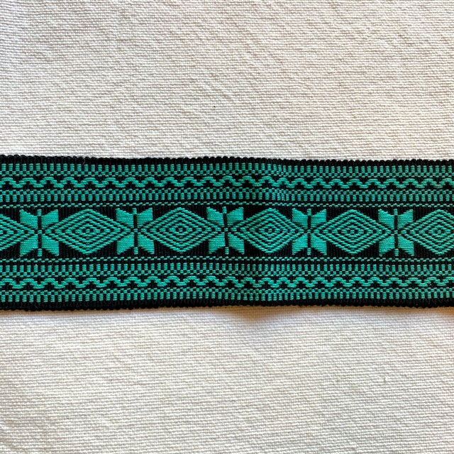 Green and black woven belt with tassels on a beige background Teal and black woven belt on a light gray fabric background Style G