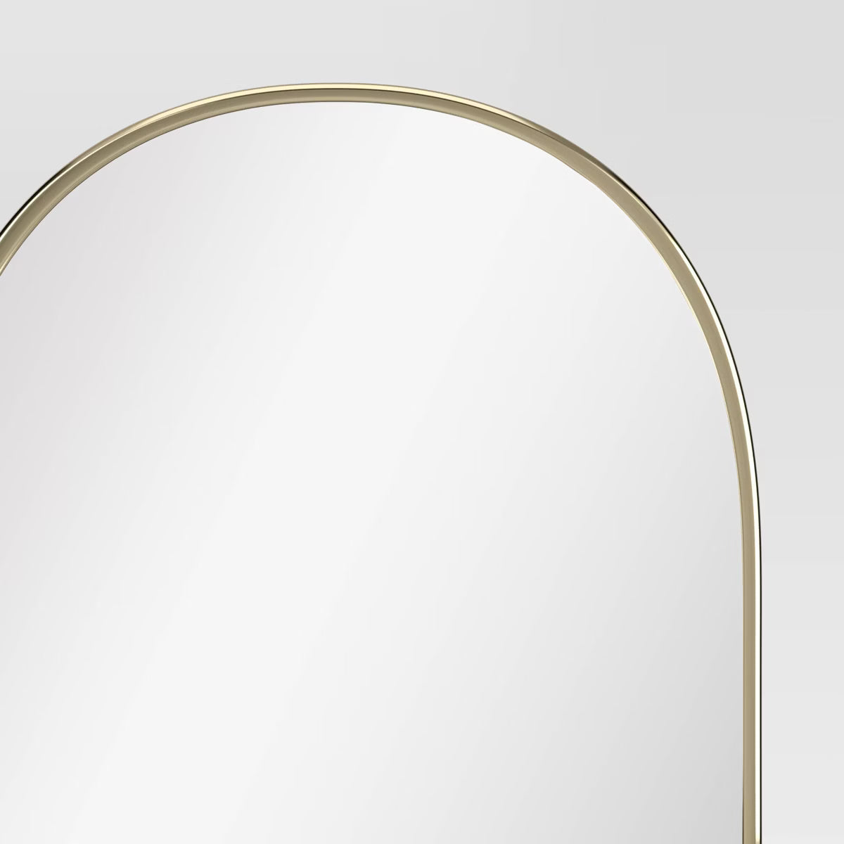 An arched mirror with a thin gold colored frame against a light gray background.