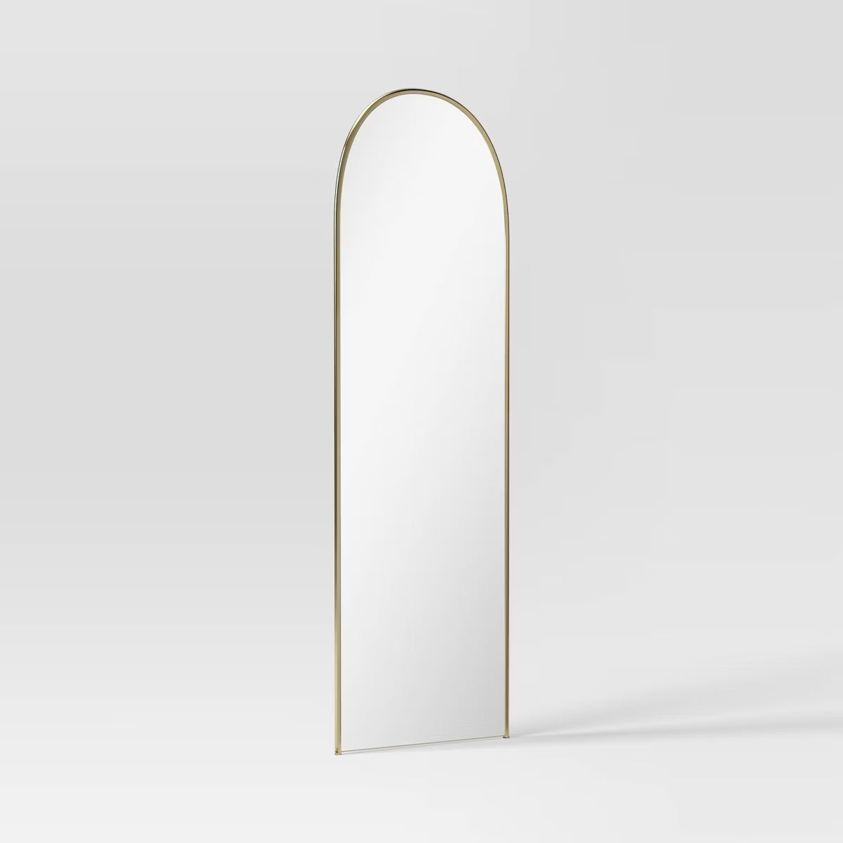 An arched mirror with a thin gold colored frame against a light gray background.