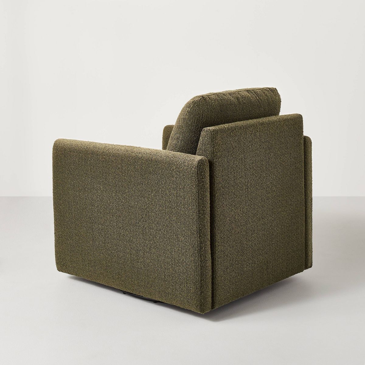 A greenish brown colored armchair with a textured fabric and square shape, placed on a light gray floor.