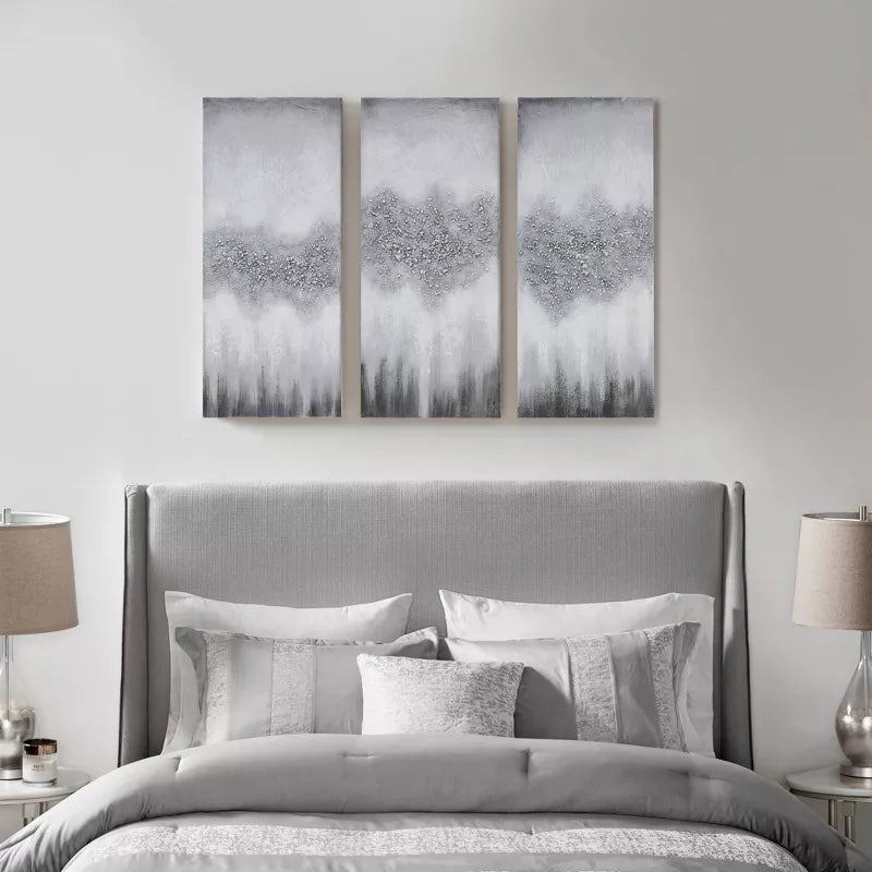 Gray upholstered bed with decorative pillows and three abstract wall art pieces above it.