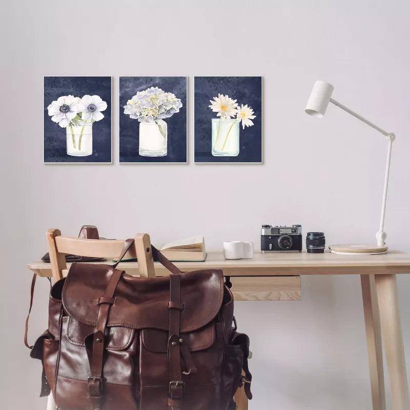 Desk with a brown leather bag, camera, and mug, featuring three floral paintings on the wall.