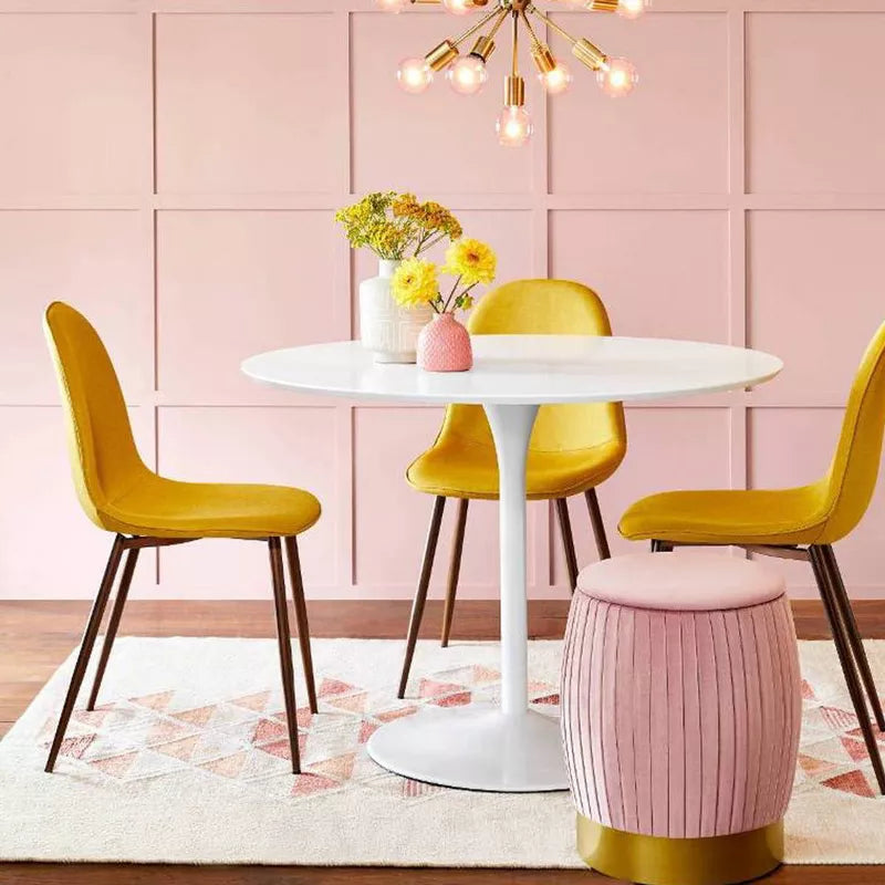 Dining room with a round white table and yellow chairs against a pink paneled wall.