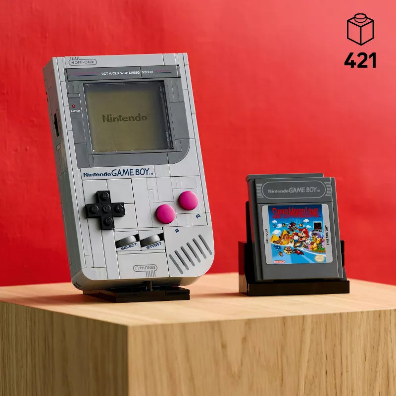 Nintendo Game Boy model with a game cartridge on a wooden surface against a red background