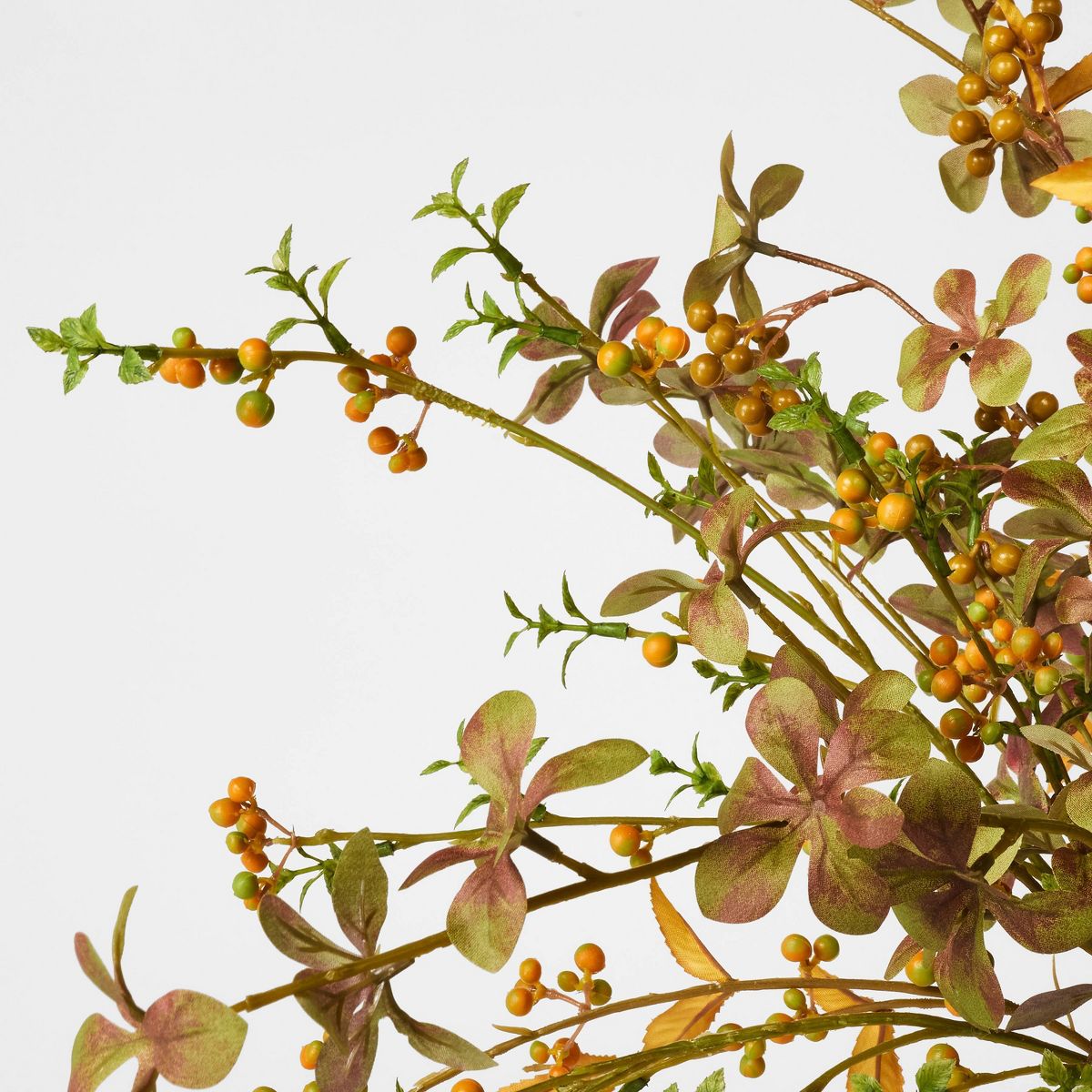 An artificial autumn leafy branch arrangement in a matte cream ceramic vase, photographed on a clean white studio background.