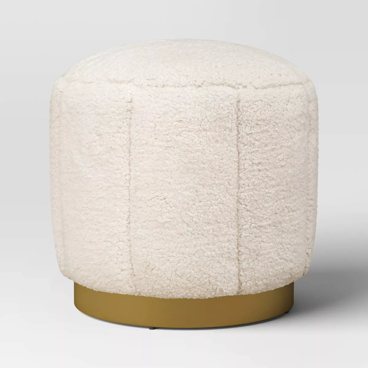 A round, cream colored ottoman with a textured surface and a gold colored base."