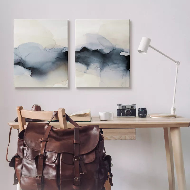 Desk with a leather backpack, camera, and books, featuring abstract wall art.