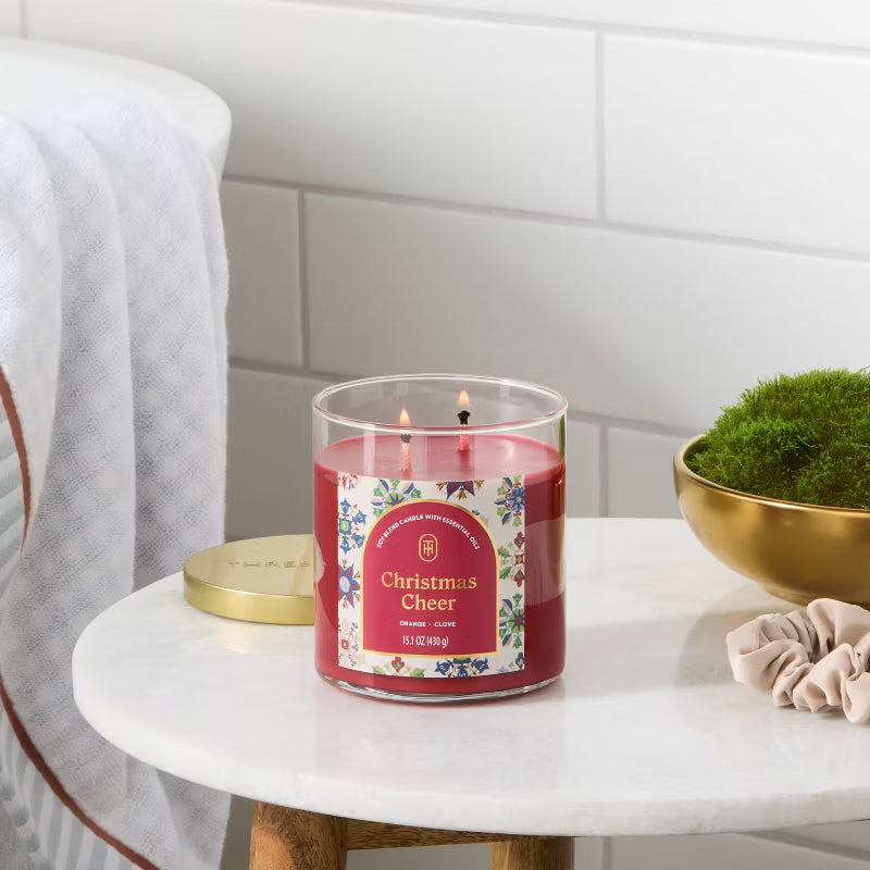Candle labeled 'Christmas Cheer' on a table with a decorative background 15.1oz