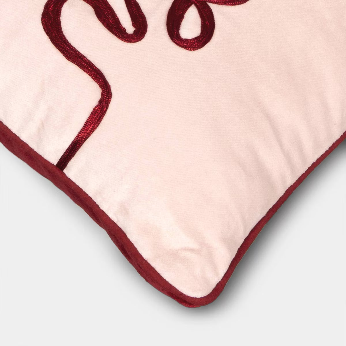 Rectangular light pink colored pillow with red colored piping and the word & quot love quot embroidered in red.